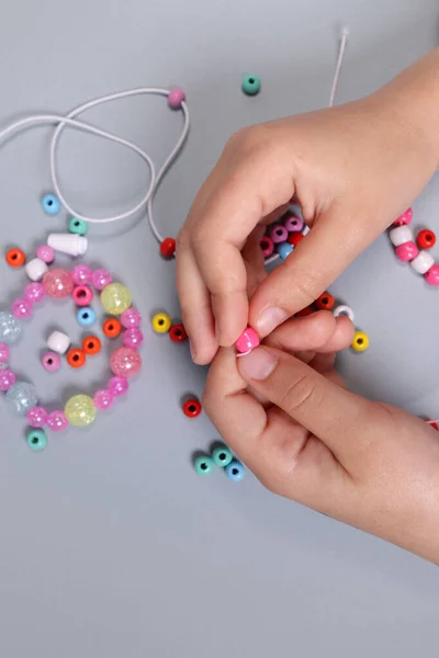 Making a bracelet from colored beads, children\'s hands close-up. vertical orientation