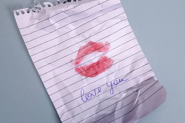Text love you and imprint of lips on a torn notepad sheet