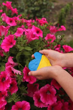 Ukrayna bayrağı çocukların ellerinde bir kalp şeklinde çiçeklerin arka planında