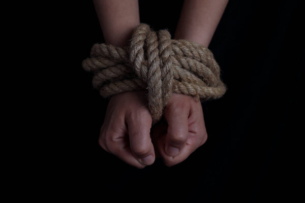 girl's hands tied with a rope on a black background