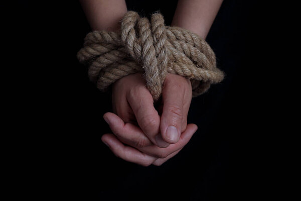 girl's hands tied with a rope on a black background