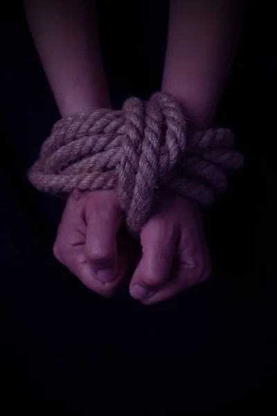 girl\'s hands tied with a rope on a black background. vertical orientation