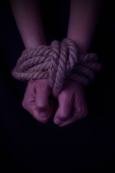 girl's hands tied with a rope on a black background. vertical orientation