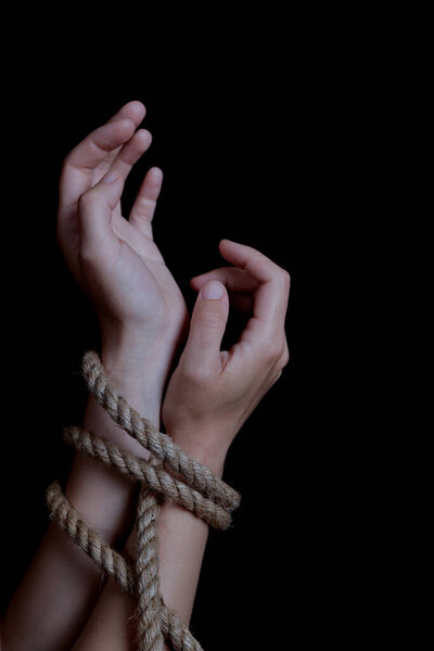 woman's hands tied with rope on black background, concept of domestic violence of the victim. vertical orientation