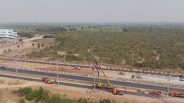 İnsansız hava aracı görüntüsü manzaralı vinçler ve tamirciler inşaat halindeki kırsal bir yol boyunca yüksek voltajlı elektrik hatlarını tamir ediyorlar.