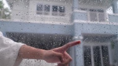 Bir insan eli, yağmura tutulmuş bir arabanın camını parmaklarıyla çiziyor.