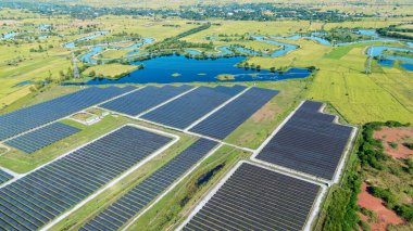 Drone 'un hava görüntüsü güneş enerjisi dizisi kırsal alanda yeşil ve suyla çevrili büyük ölçekli bir tesiste yenilenebilir enerji sağlıyor. Kırsaldaki güneş çiftliği