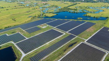 Drone 'un hava görüntüsü güneş enerjisi dizisi kırsal alanda yeşil ve suyla çevrili büyük ölçekli bir tesiste yenilenebilir enerji sağlıyor. Kırsaldaki güneş çiftliği