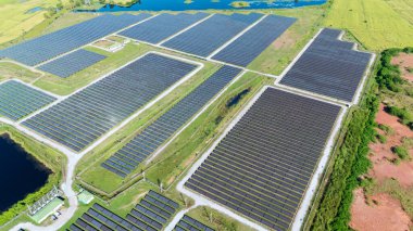 Drone 'un hava görüntüsü güneş enerjisi dizisi kırsal alanda yeşil ve suyla çevrili büyük ölçekli bir tesiste yenilenebilir enerji sağlıyor. Kırsaldaki güneş çiftliği
