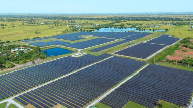 Drone 'un hava görüntüsü güneş enerjisi dizisi kırsal alanda yeşil ve suyla çevrili büyük ölçekli bir tesiste yenilenebilir enerji sağlıyor. Kırsaldaki güneş çiftliği