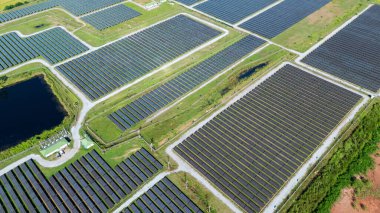 Drone 'un hava görüntüsü güneş enerjisi dizisi kırsal alanda yeşil ve suyla çevrili büyük ölçekli bir tesiste yenilenebilir enerji sağlıyor. Kırsaldaki güneş çiftliği