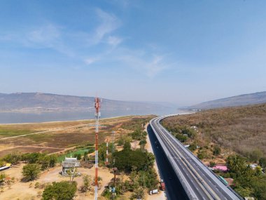İHA görüntülü iletişim kulesi, açık havada nehir ve tepelerle manzaralı otoyola bakan yüksek bir yerde duruyor.