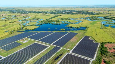 Drone 'un hava görüntüsü güneş enerjisi dizisi kırsal alanda yeşil ve suyla çevrili büyük ölçekli bir tesiste yenilenebilir enerji sağlıyor. Kırsaldaki güneş çiftliği