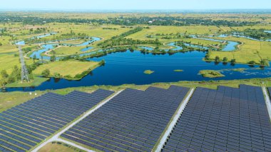 Drone 'un hava görüntüsü güneş enerjisi dizisi kırsal alanda yeşil ve suyla çevrili büyük ölçekli bir tesiste yenilenebilir enerji sağlıyor. Kırsaldaki güneş çiftliği