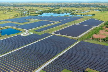 Drone 'un hava görüntüsü güneş enerjisi dizisi kırsal alanda yeşil ve suyla çevrili büyük ölçekli bir tesiste yenilenebilir enerji sağlıyor. Kırsaldaki güneş çiftliği