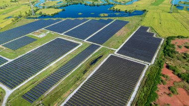 Drone 'un hava görüntüsü güneş enerjisi dizisi kırsal alanda yeşil ve suyla çevrili büyük ölçekli bir tesiste yenilenebilir enerji sağlıyor. Kırsaldaki güneş çiftliği