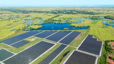 Drone 'un hava görüntüsü güneş enerjisi dizisi kırsal alanda yeşil ve suyla çevrili büyük ölçekli bir tesiste yenilenebilir enerji sağlıyor. Kırsaldaki güneş çiftliği