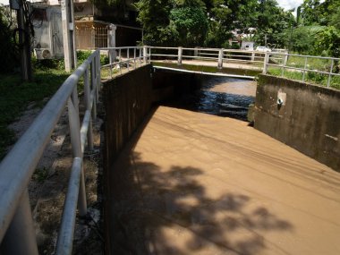 Ağaçlarla çevrili ve suyu yansıtan, kızıl su nehri üzerindeki bir köprüyü barındıran sakin, yağmurlu bir manzara.