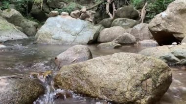 Kayalar nehir yatağından yayılır, etraflarında yavaşça akan su dalgalanmalar yaratır ve doğal güzelliği yansıtır. 4k video kaydı