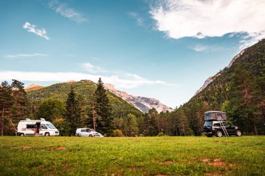 Gün batımında ormanın ve dağların muhteşem manzarasına sahip bir vadideki çeşitli karavan araçları. Minibüs tatili ve açık hava yaz macerası. Göçebe yaşam tarzı konsepti