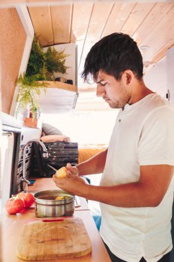 Genç adam karavanının mutfağında yemek hazırlıyor. Minibüs tatili ve açık hava yaz macerası. Göçebe yaşam tarzı konsepti