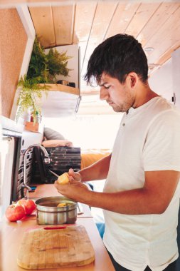 Young man preparing meal in the kitchen of his camper van. Van road trip holiday and outdoor summer adventure. Nomad lifestyle concept clipart