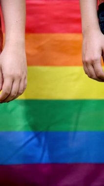 Lezbiyen bir çiftin arka planda canlı bir gökkuşağı gurur bayrağıyla el ele tutuşup LGBTQ + gurur ve kapsayıcılığı temsil ettiği yavaş çekim videosunu kapatın.