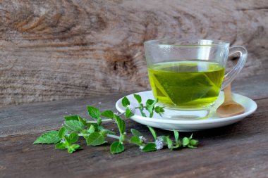 Bir fincan nane çayı ve ahşap masanın üzerinde nane yaprakları..