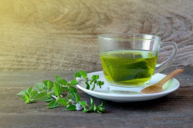 Bir fincan nane çayı ve ahşap masanın üzerinde nane yaprakları..