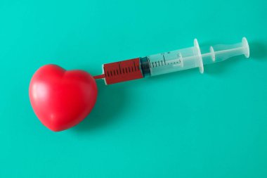 Kırmızı kalbe takılmış kırmızı sıvılı tıbbi şırınga..