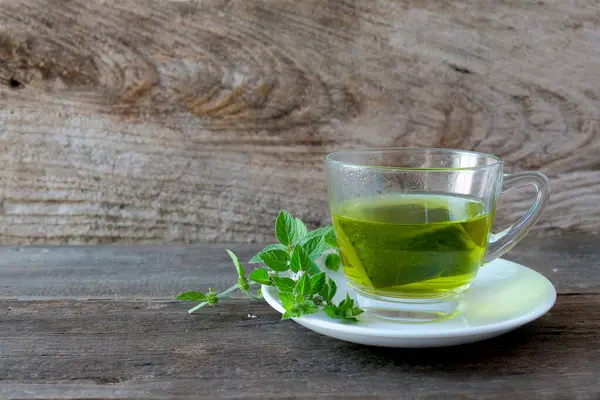 Bir fincan nane çayı ve ahşap masanın üzerinde nane yaprakları..