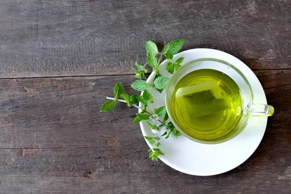 Bir fincan nane çayı ve ahşap masanın üzerinde nane yaprakları..
