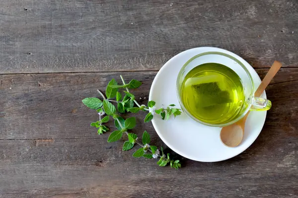 Bir fincan nane çayı ve ahşap masanın üzerinde nane yaprakları..
