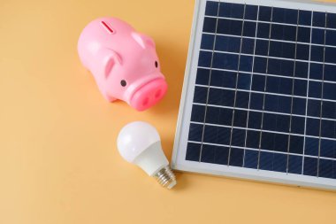 Arka planda güneş paneli ve domuz kumbarası bileşimi.