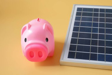 Arka planda güneş paneli ve domuz kumbarası bileşimi.