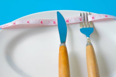 Çatal ve bıçak, beyaz tabakların etrafında mezura. Sağlık konsepti..