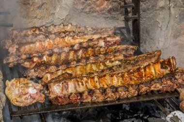Büyük bir barbeküde ahşap ateşle biftek, pirzola sosisi pişiriyorum.