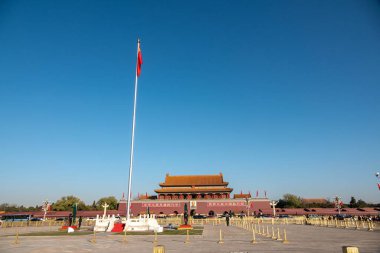 Pekin 'deki Uçsuz bucaksız Tiananmen Meydanı' nda parlak mavi gökyüzüne karşı dalgalanan belirgin kırmızı bayraklar görülüyor..