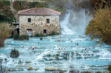 Ziyaretçiler Cascate del Mulino 'nun sıcak, kaynayan sularının tadını çıkarırken büyüleyici doğal güzelliklerle çevrelenmiş durumdalar..
