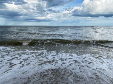 Dalgalı ve deniz kabarcıklı kumsalda kimse yok. Rüzgarlı bir arka plan görüntüsünde büyük bir dalga. Güzel bir deniz manzarası..