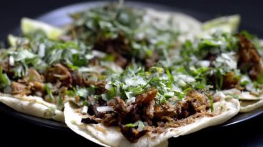 Siyah bir arka planda siyah bir tabakta Meksika carnitas tacolarının üzerine yeşil salsa verde dökülüyordu. Kişniş soğanlı, limonlu ve baharatlı yeşil soslu gurme domuz tacoları..
