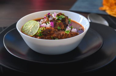 Siyah tabakta kırmızı Meksika bifteği güveci ile dolu beyaz kase. Kırmızı soğan, kişniş ve limonla servis edilir. Geleneksel olarak Jalisco ve Orta Meksika eyaletlerinden..