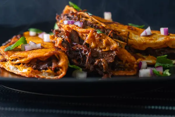 Siyah bir tabakta istiflenmiş 3 gevrek, sulu biftek birria taco. Tijuana, Meksika 'da inanılmaz Meksika yemeklerinin iştah açıcı düzeni..