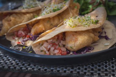 Lezzetli Meksika usulü balıklı taco. Yumuşak mısır tortillası üzerine pico de gallo ile kızartılmış altın balık. Siyah bir tabakta servis edildi..