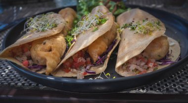 Lezzetli Meksika usulü balıklı taco. Yumuşak mısır tortillası üzerine pico de gallo ile kızartılmış altın balık. Siyah bir tabakta servis edildi..