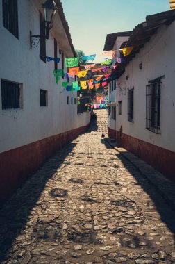 Tipik bir Meksika caddesi. Kağıttan Picado bayrakları kaldırım taşından yola gölge düşürüyor. Valle de Bravo, Meksika Eyaleti..