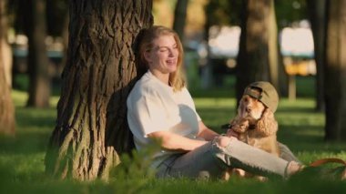 Şehir parkında köpeğiyle eğlenen genç bir kadın. Kız, İngiliz Cocker Spaniel Dog 'a şapka takıyor.