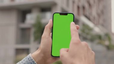 Şehrin arka planında, erkeklerin elinde dikey yeşil ekranlı telefonu kapat. Adam dışarıda Smartphone kullanıyor, Krom Anahtar Görünümünde Parşömenler ve Dokunuşlar