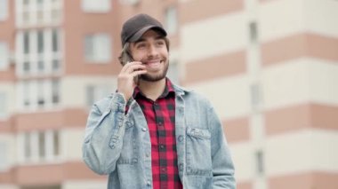 Neşeli ruh hali içindeki genç adam telefonda konuşuyor ve caddede yürürken gülümsüyor.