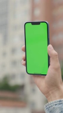 Şehrin arka planında, erkeklerin elinde dikey yeşil ekranlı telefonu kapat. Adam dışarıda Smartphone kullanıyor, Krom Anahtar Ekranında Parşömenler ve Dokunuşlar. Dikey Video